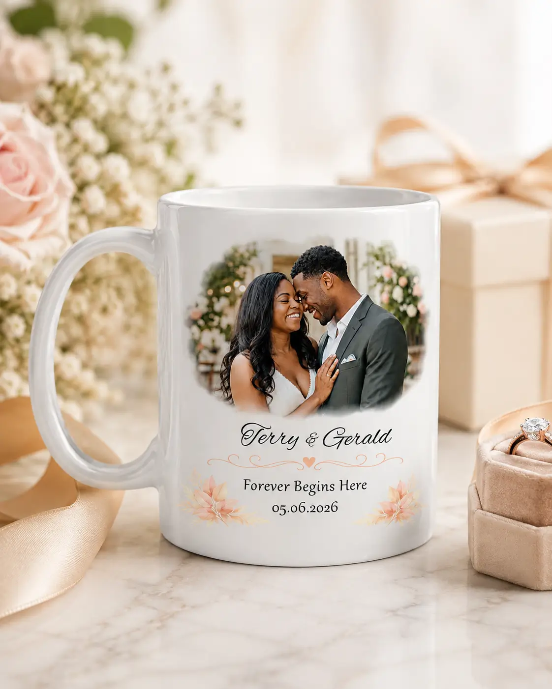Lifestyle mockup of a personalized wedding photo mug with floral styling, ribbon, ring box, and gift box on a marble surface